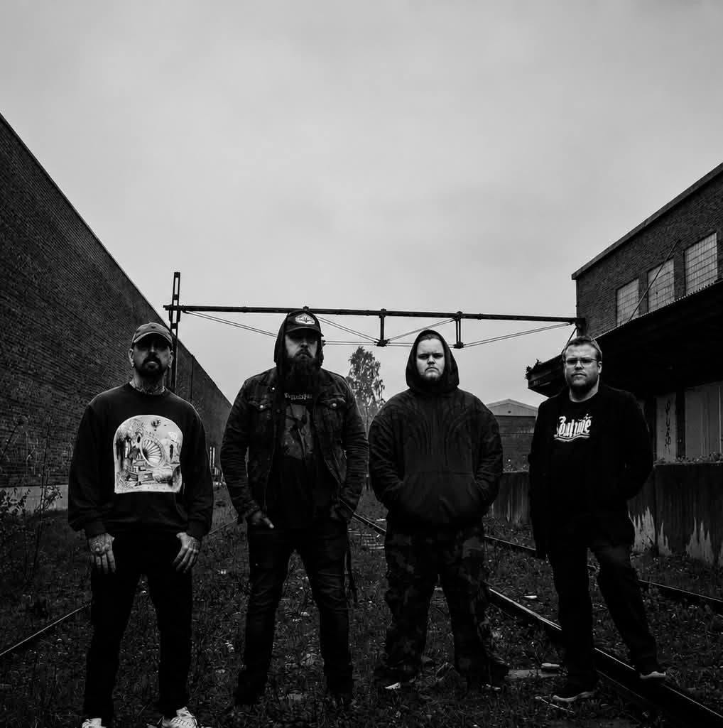 The four members of Among The Pestilence standing on a railway track between brick buildings